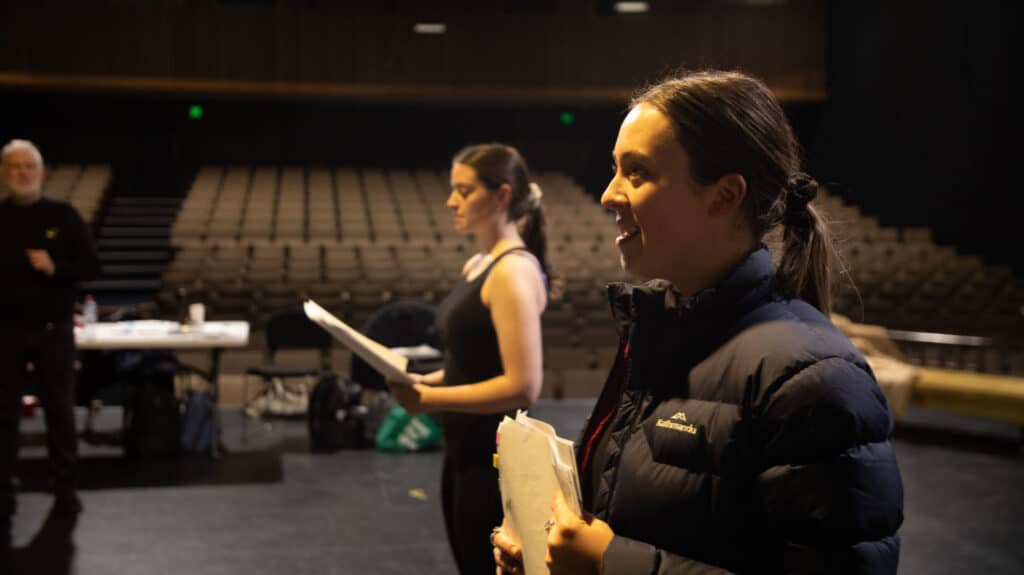Zoe Mills and Ella Le Fournour rehearsing on the stage of the Matthew Flinders Theatre with director Wayne Harrison AM Flinders Drama Centre1